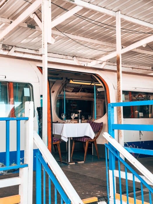 Outside of an old disused Victoria Line tube carriage with a fine-dining table inside one of the doors at Walthamstow Supperclub, London