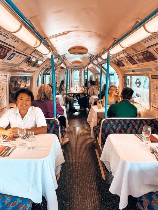 Andy sitting inside the vintage Victoria Line tube carriage with lots of other tables and chairs with people sat at, Walthamstow Supperclub, London Restaurant