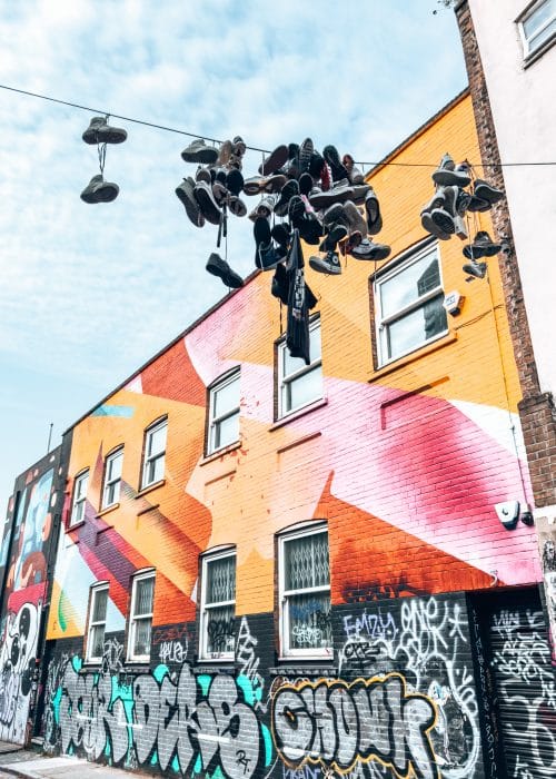 A colourful wall with several shoes hanging above it, Shoreditch Street Art, 4 Day London Itinerary