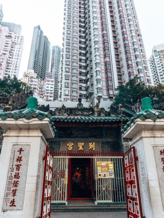 The beautiful and colourful exterior of Man Mo Temple with huge skyscrapers towering above behind it, things to do in Hong Kong