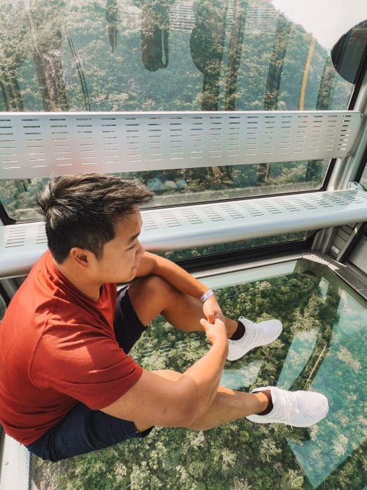 Andy sat on the glass bottom floor of a cable car above a forest, Ngong Ping 360, Lantau Island, Hong Kong Itinerary