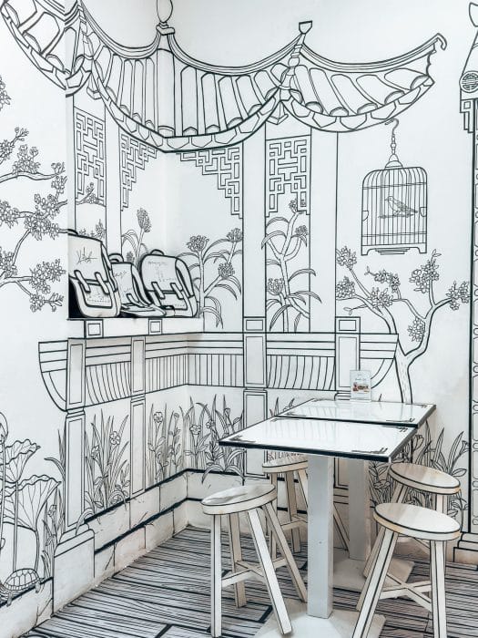 A black and white table and chairs in front of a decorative wall at 2D Cafe, Chinatown, Singapore itinerary