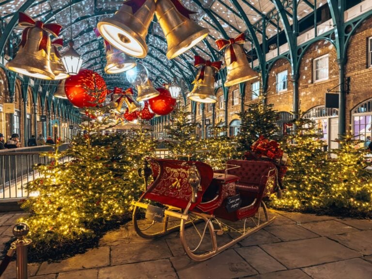 Santa's sleigh in front of several Christmas trees underneath giant gold bells and red bows, Covent Garden at Christmas