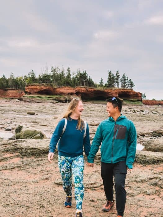 Helen and Andy walking on the ocean floor with red rocks behind them at Burntcoat Head Park, Things to Do in Nova Scotia, Canada
