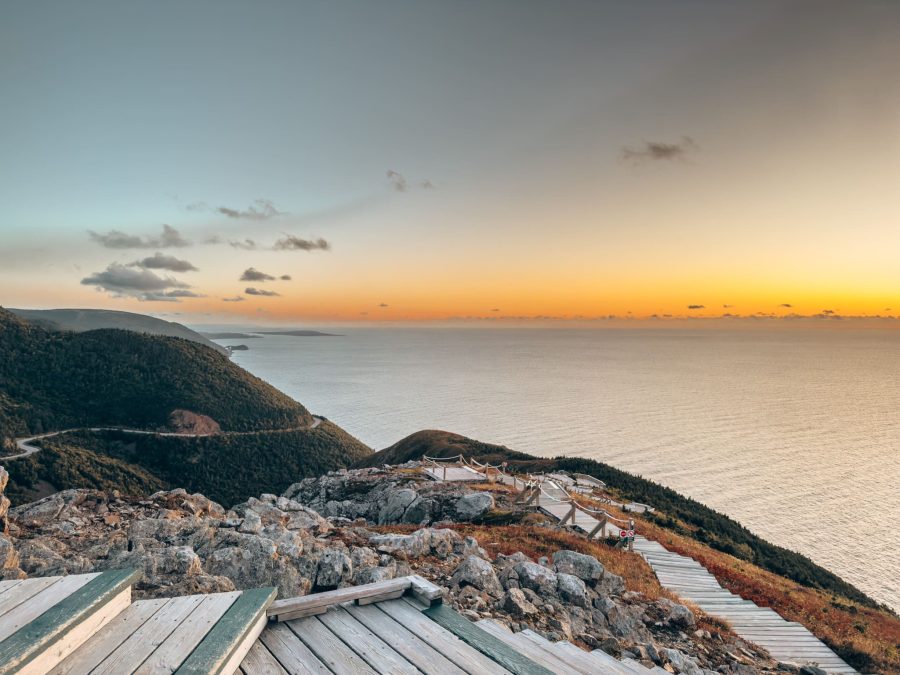 Sun lit up in a fiery glow behind the Atlantic Ocean with the Cabot Trail winding around the mountain, beautiful places to visit in Nova Scotia